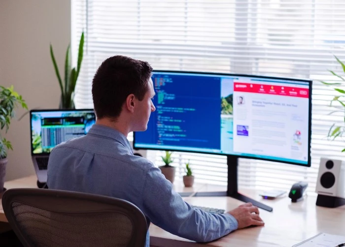 A man working on a laptop with 2 external monitors.